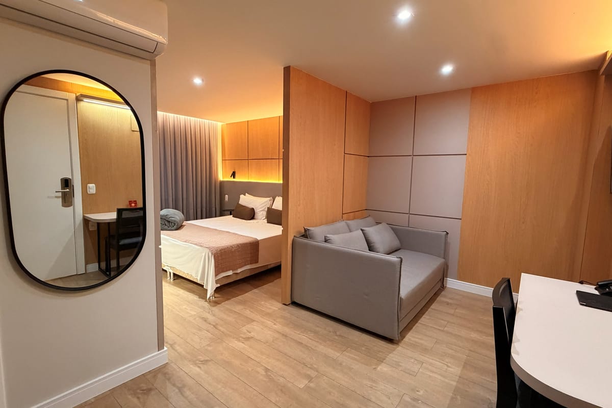 Entrada do apartamento Superior, com espelho touch, cama de casal e sofá cama ao fundo