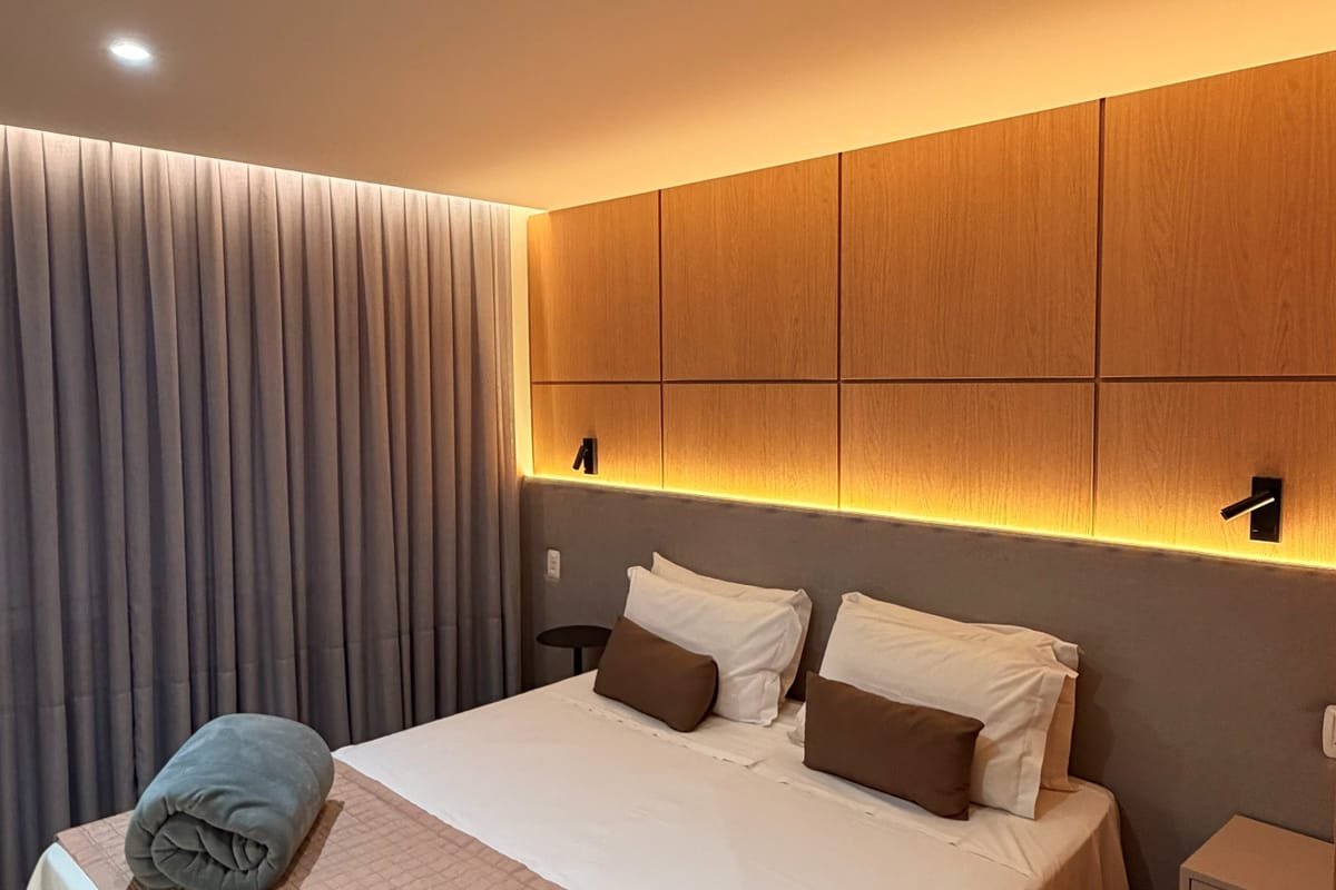 Cama de casal do apartamento Superior, com cabeceira iluminada e cortina blackout